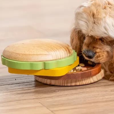 Thumbnail 400x400 for Un perro pequeño y peludo huele e interactúa con el juguete de madera en forma de hamburguesa apilada sobre un suelo de madera.